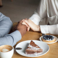 Interracial couple holding hands sit at cafe table, african black man and white woman in love enjoy date in coffee house concept, romantic biracial lovers meet in public place together, close up view